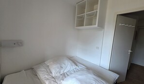 Ein Schlafzimmer mit einem Bett, einer weißen Wand, einer Tür und einem weißen Regal.