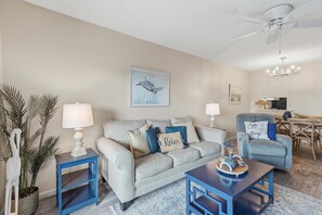 A living room with a sofa, two side tables, a coffee table, and a dining area with a chair and table. - Sea Coast Gardens II 511 (New Smyrna Beach)