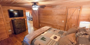 A wooden-paneled room with a bed, a dresser, a television, and a ceiling fan. - Cozy 3-bedroom cabin in gorgeous Little River Canyon with Hot tub (Fort Payne)