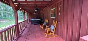 A covered porch with a hot tub, wooden rocking chairs, and a view of the forest. - Cozy 3-bedroom cabin in gorgeous Little River Canyon with Hot tub (Fort Payne)