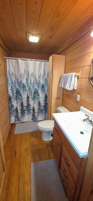 A compact wooden bathroom with a toilet, sink, and shower curtain. - Cozy 3-bedroom cabin in gorgeous Little River Canyon with Hot tub (Fort Payne)