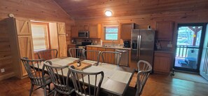 A wooden cabin kitchen with a dining table, chairs, a refrigerator, and a microwave. - Cozy 3-bedroom cabin in gorgeous Little River Canyon with Hot tub (Fort Payne)