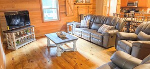 A cozy living room with a leather sofa, a television, and a coffee table. - Cozy 3-bedroom cabin in gorgeous Little River Canyon with Hot tub (Fort Payne)