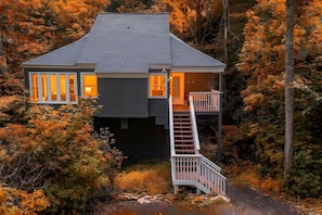 A two-story cabin with a wooden staircase leading to a balcony, surrounded by autumn foliage. - Updated 3 BR Chalet/Walk to Sugar Mountain Resort/ Hot tub/ Fireplace (Sugar Mountain)