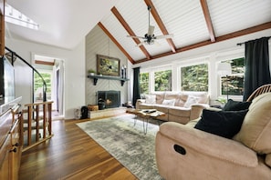 A spacious living room with a fireplace, wooden beams, a sofa, and a staircase. - Updated 3 BR Chalet/Walk to Sugar Mountain Resort/ Hot tub/ Fireplace (Sugar Mountain)