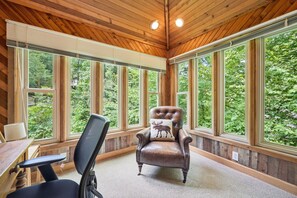 A room with large windows, a leather chair, a desk, and a chair.