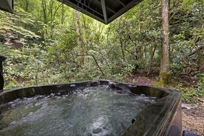 Ein Whirlpool in bewaldeter Landschaft mit einer überdachten Holzterrasse.