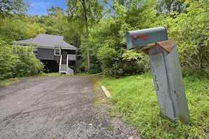 A house with a driveway leading to a front door, surrounded by dense greenery. - Updated 3 BR Chalet/Walk to Sugar Mountain Resort/ Hot tub/ Fireplace (Sugar Mountain)