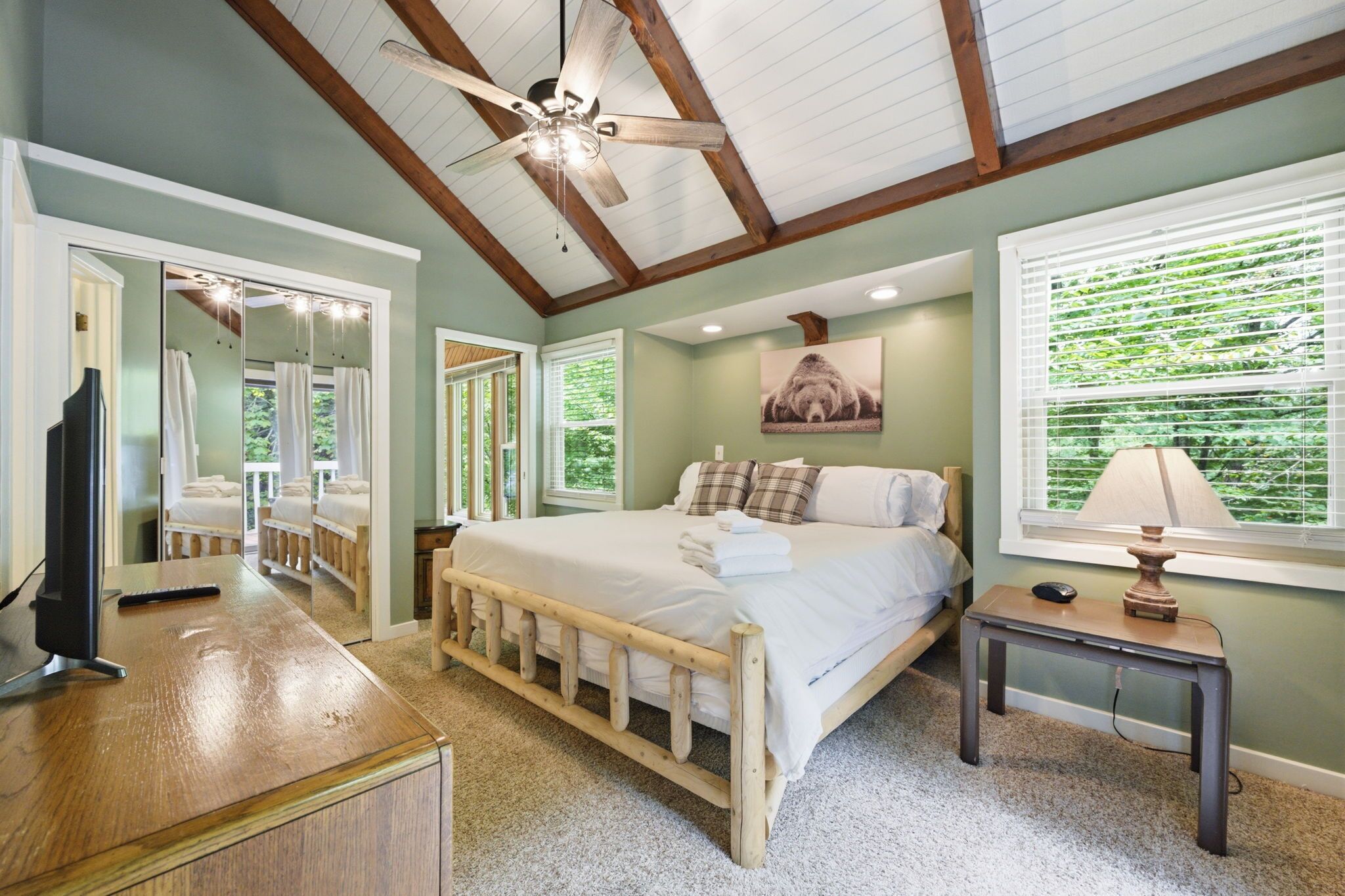 A bedroom with a bed, a desk, a chair, a ceiling fan, and a window with blinds.