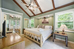A bedroom with a bed, a desk, a chair, a ceiling fan, and a window with blinds.