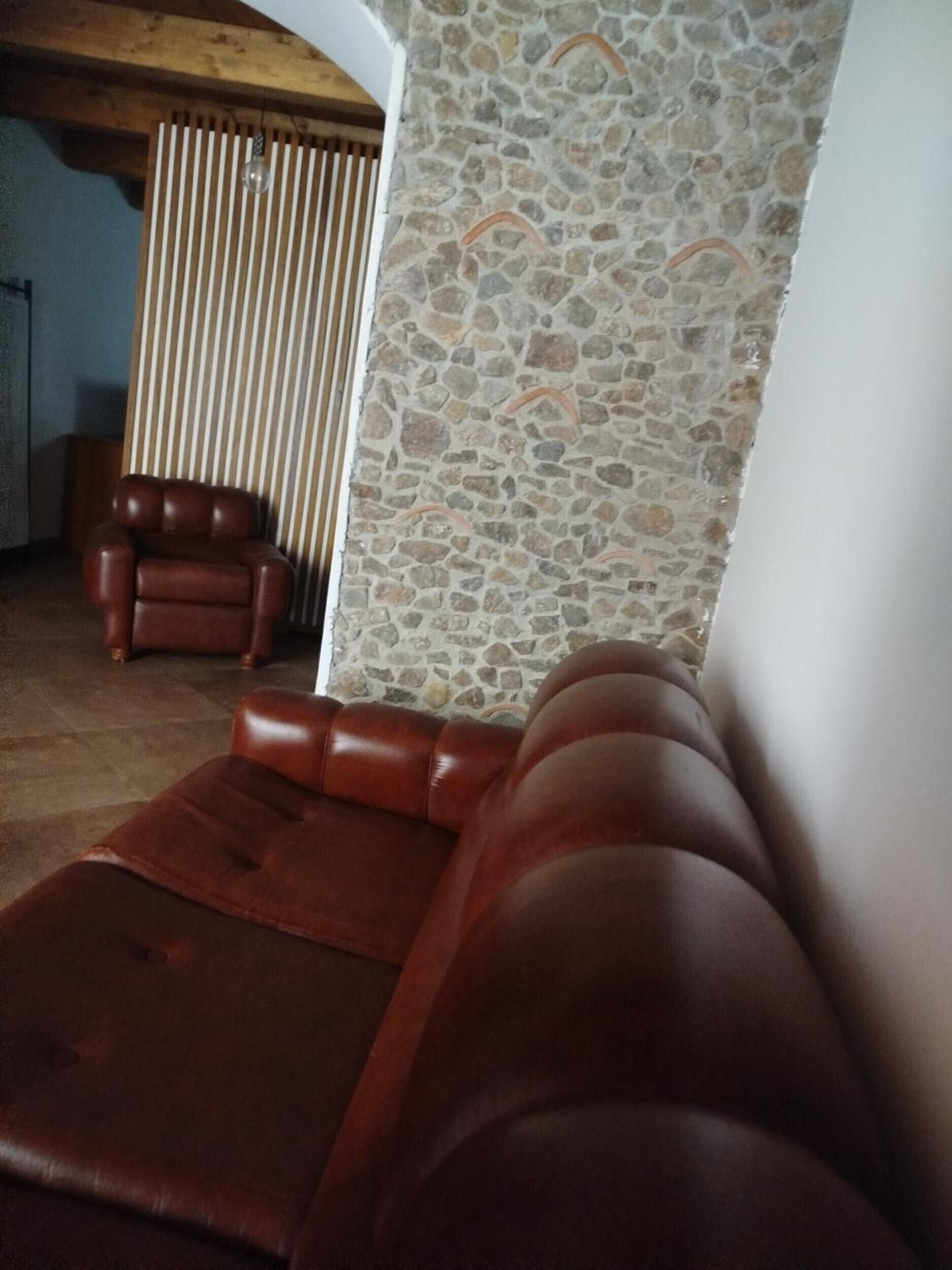 A room with a stone wall, a wooden ceiling, and a brown leather sofa.