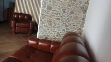 A room with a stone wall, a wooden ceiling, and a brown leather sofa.
