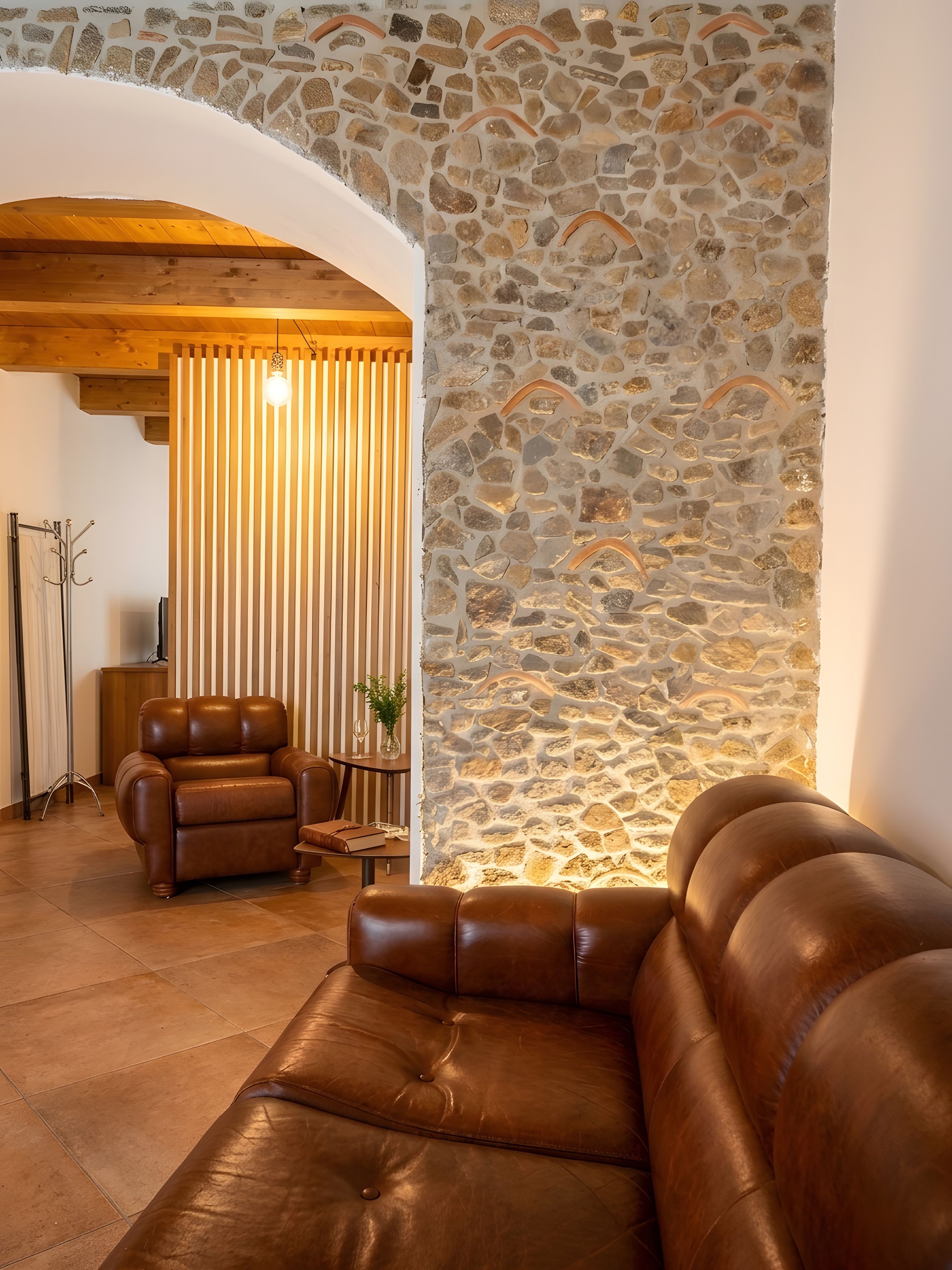 A room with a stone wall, leather sofas, and a wooden ceiling.