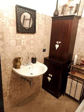 Un bagno con lavandino, specchio e mobile contenitore in legno scuro con cuori decorativi.
