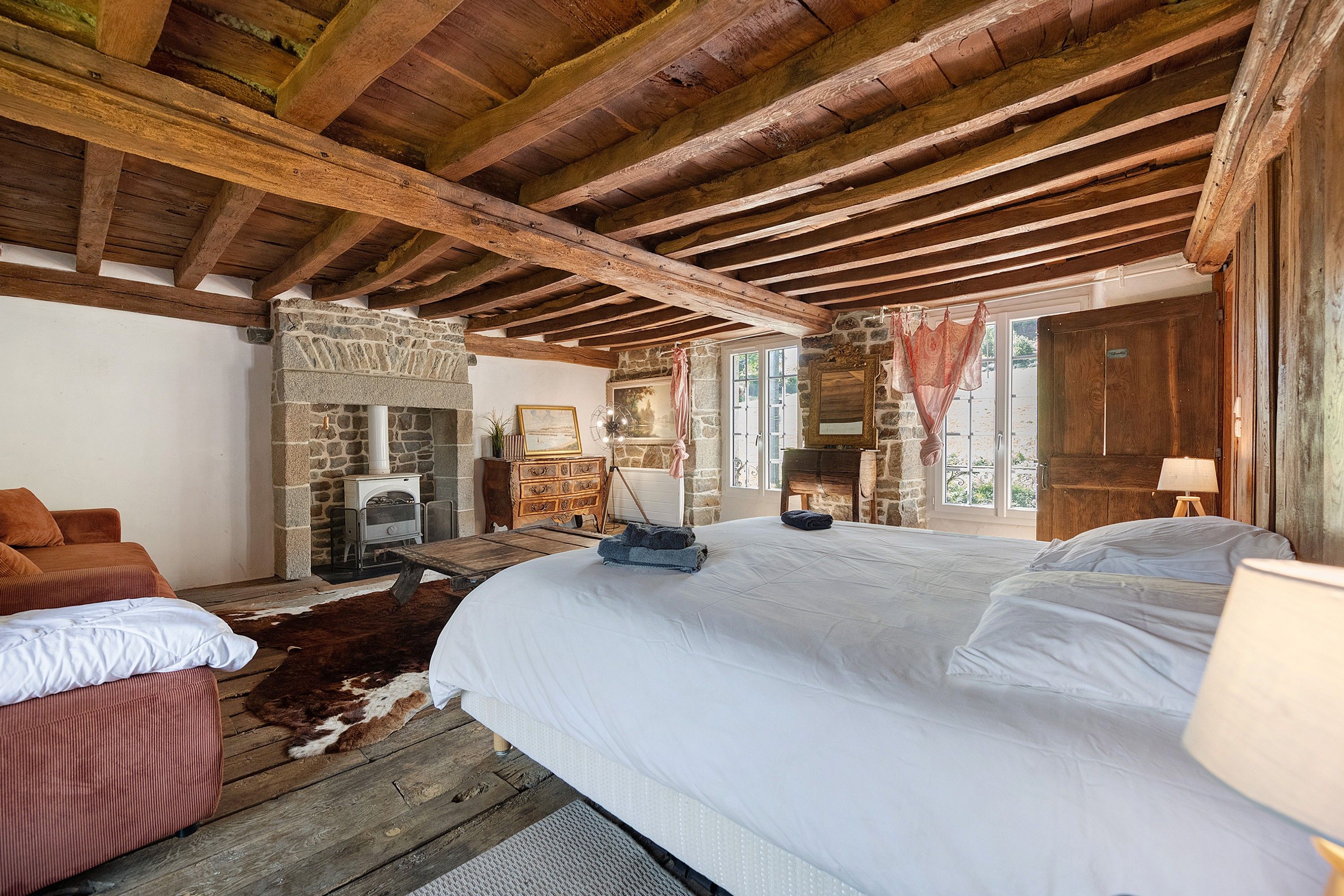 Ein rustikales Schlafzimmer mit einem großen Bett, einem Steinkamin und Holzbalken an der Decke.