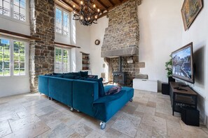 A spacious living room with a large blue sofa, a stone fireplace, and a television on a stand.