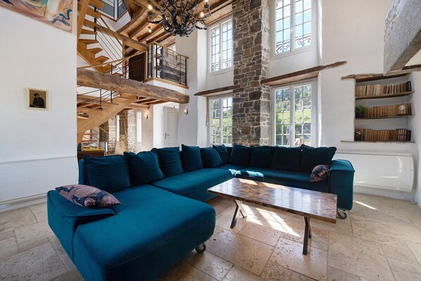 A spacious living room with a large teal sectional sofa, a wooden coffee table, and a stone fireplace.
