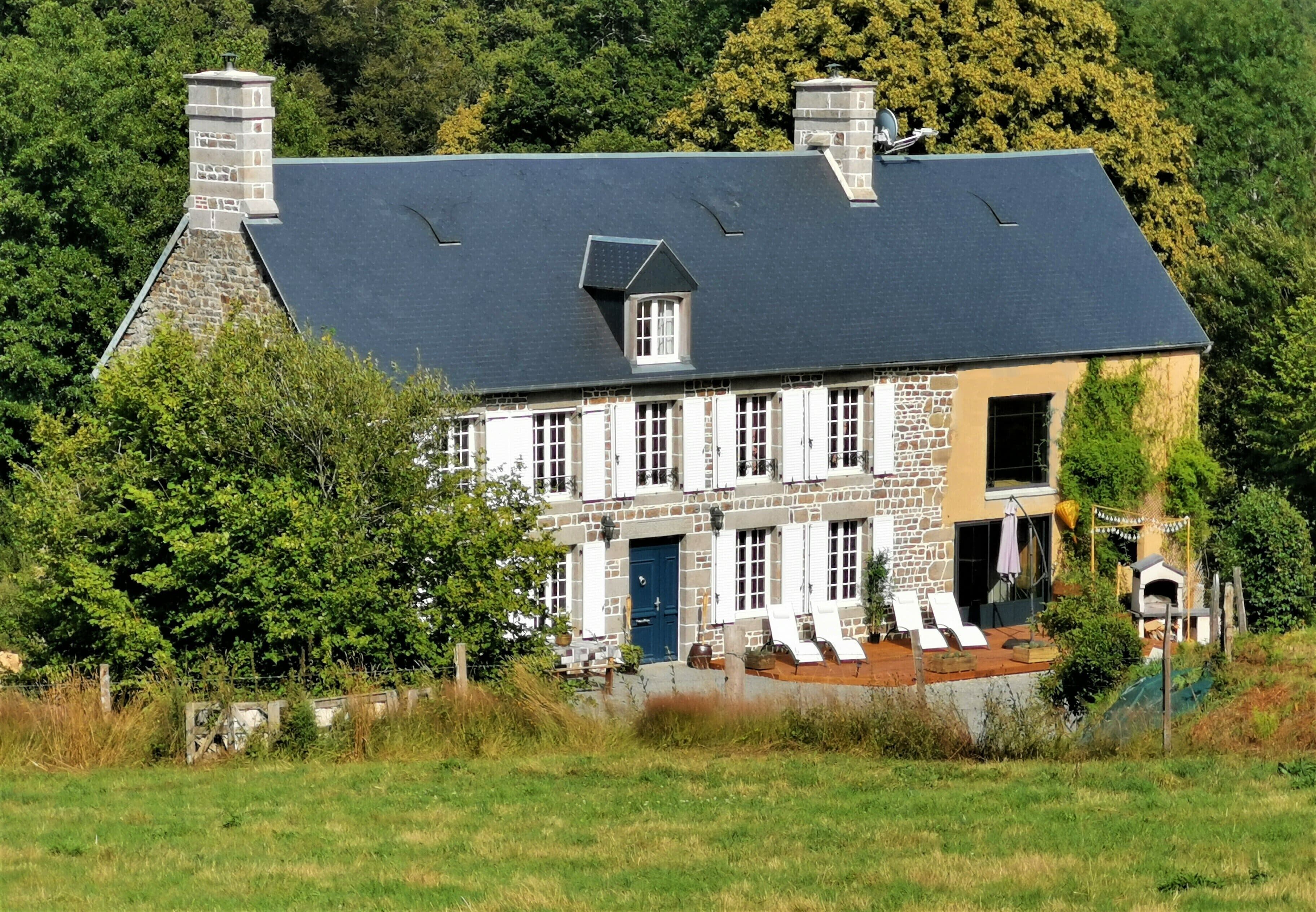 A two-story stone house with a dark roof, white shutters, and a small porch with chairs.