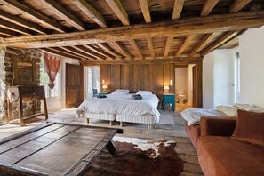 A rustic bedroom with a wooden ceiling, a large bed, a wooden table, and a cowhide rug.