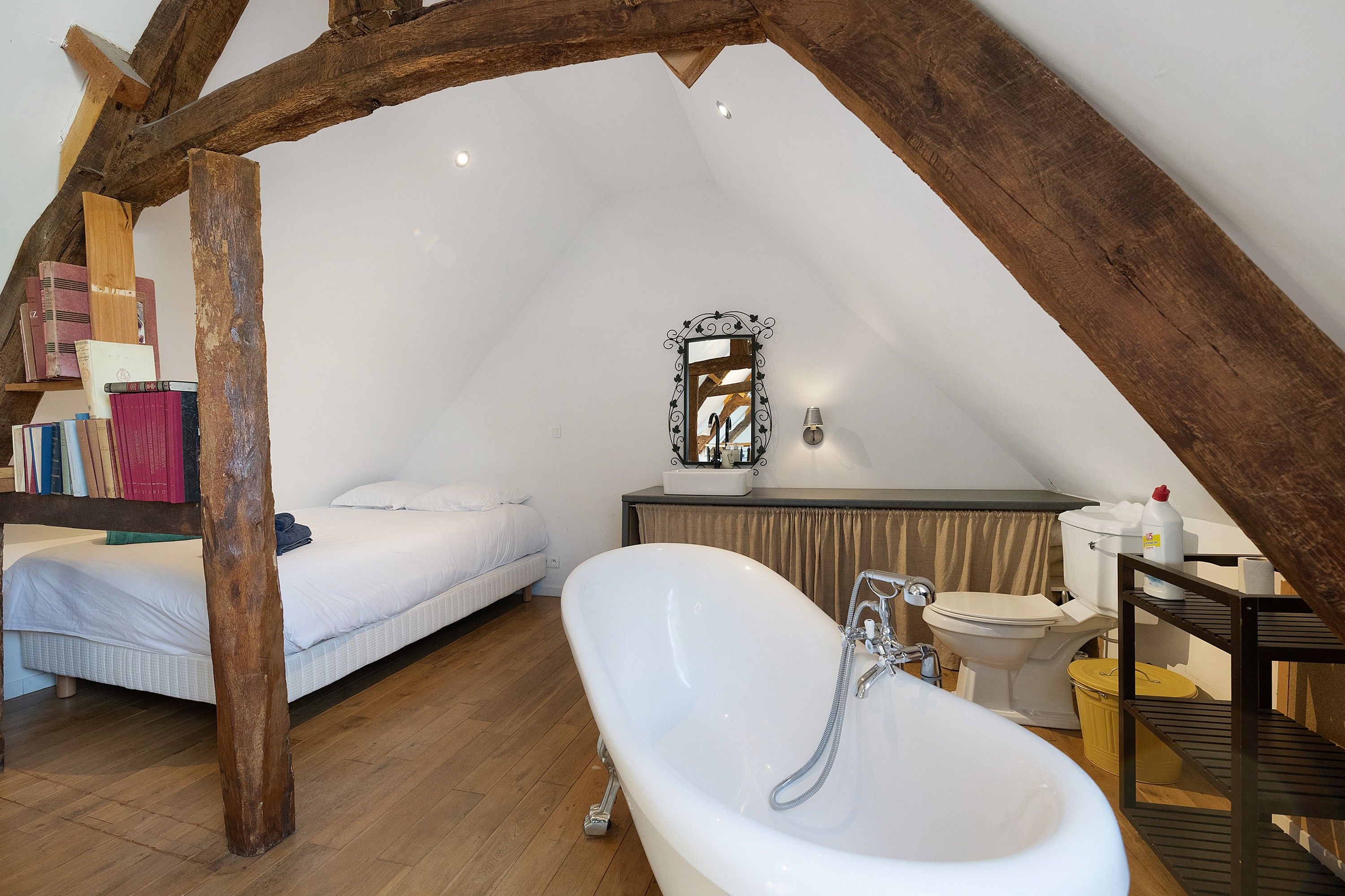 Ein Schlafzimmer mit schrägem Dach, einem Einzelbett, einem Schminktisch mit Spiegel und einer Badewanne.