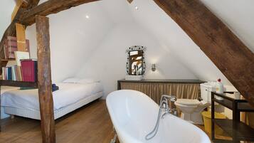 Ein Schlafzimmer mit schrägem Dach, einem Einzelbett, einem Schminktisch mit Spiegel und einer Badewanne.