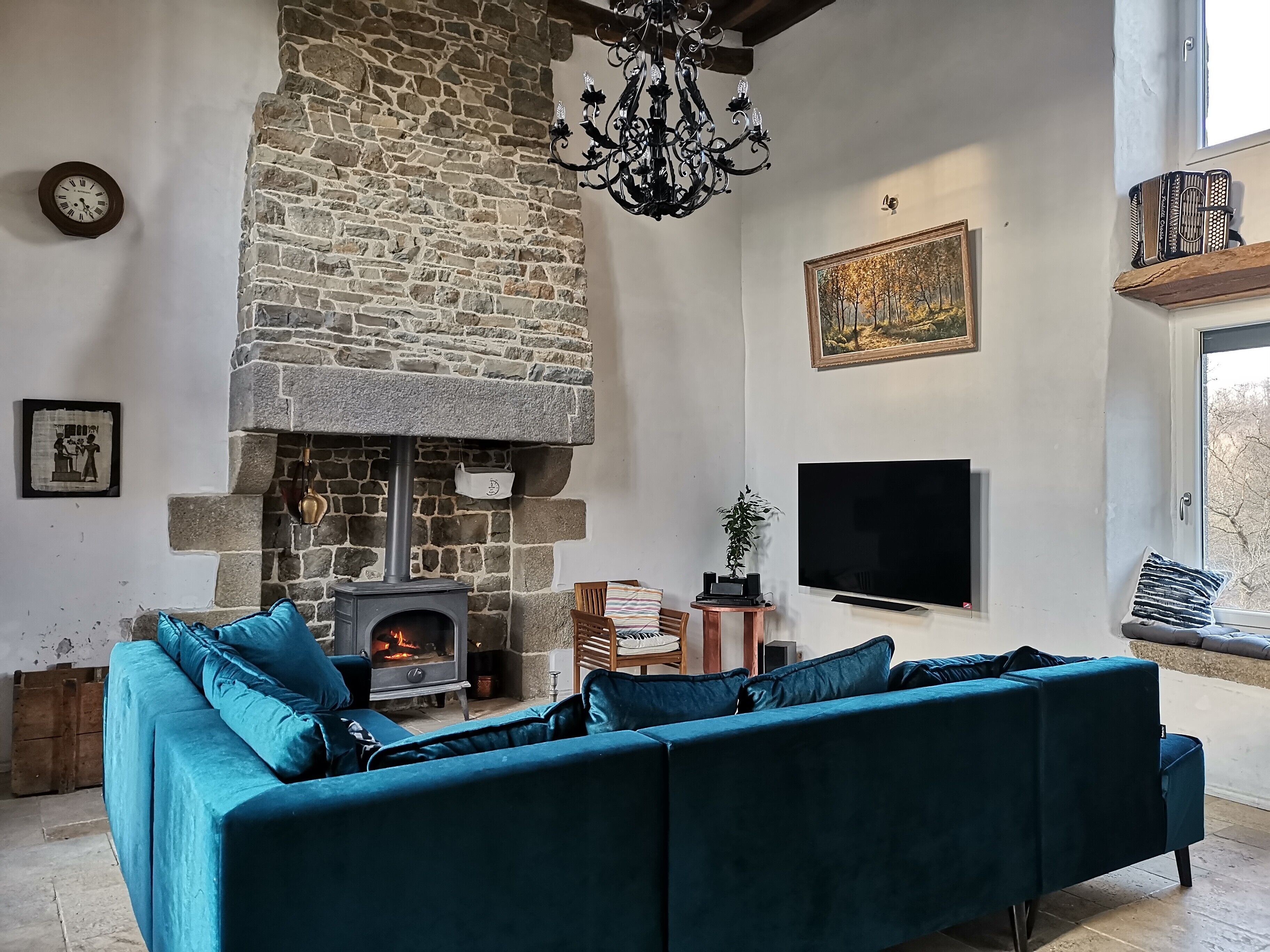 A cozy living room with a stone fireplace, a large flat-screen TV, and a teal sofa.