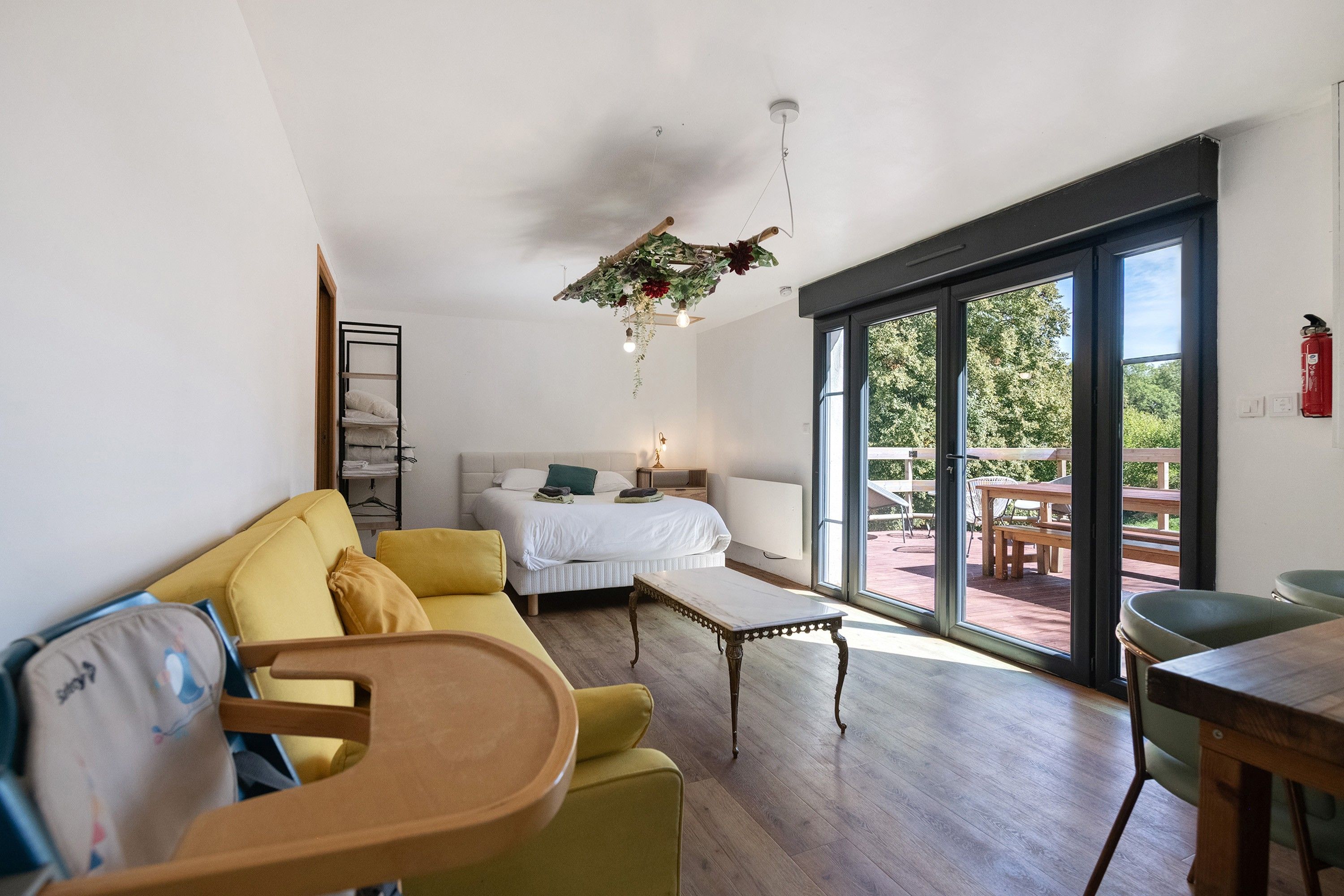 Ein modernes Wohnzimmer mit einer Couch, einem Bett, einem Esstisch und Blick ins Freie durch große Schiebetüren.