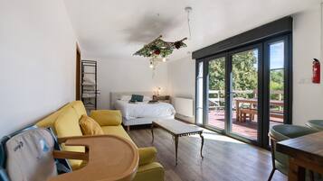 Ein modernes Wohnzimmer mit einer Couch, einem Bett, einem Esstisch und Blick ins Freie durch große Schiebetüren.