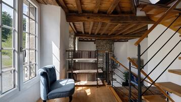 A room with a wooden ceiling, a chair, a staircase, and a bookshelf.