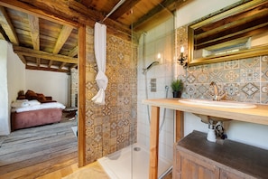 A bathroom with a wooden ceiling, a shower, a sink with a decorative mirror, and a patterned tile wall.