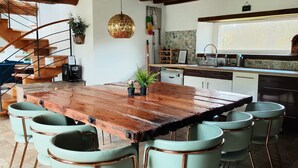 Une cuisine rustique avec une table en bois et des chaises vertes, un escalier et un mur recouvert de carreaux.