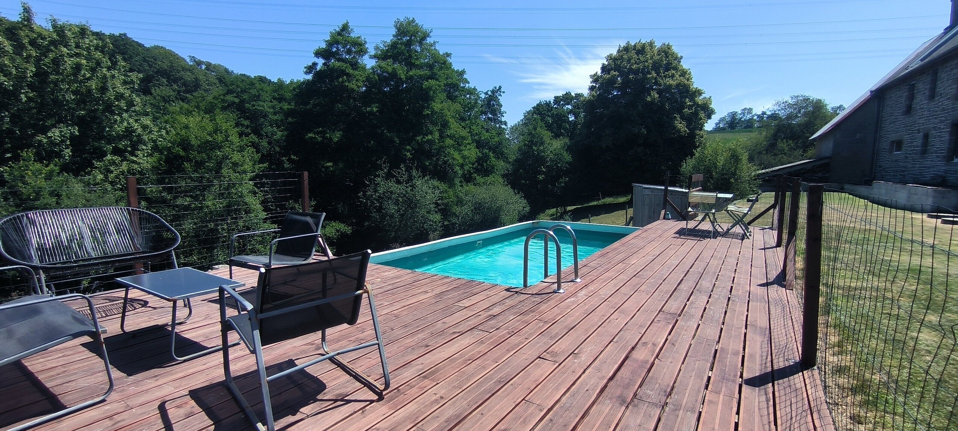 A wooden deck with a swimming pool, surrounded by trees and a stone building.