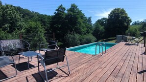 Une terrasse en bois avec une piscine, entourée d’arbres et d’un bâtiment en pierre.