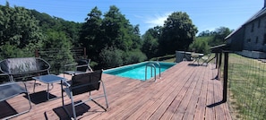 A wooden deck with a swimming pool, surrounded by trees and a stone building. - Domaine LVD Country House – Ideal for Events, Private Pool, Terrace & Wi-Fi (La Bloutière)