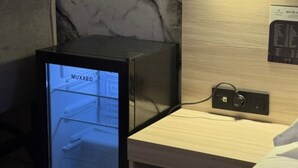 Un minibar con pantalla digital, una mesita de noche de madera y un panel de control en la pared.