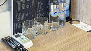 Una habitación de hotel con un menú en pizarra, dos botellas de agua, un control remoto y una copa.