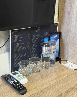A hotel room with a blackboard menu, two bottles of water, a remote control, and a glass. - VanParkHotel (Shymkent)
