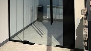 Una habitación moderna con una puerta de cristal que da a un pasillo, una escalera de madera y un pequeño cubo de basura.