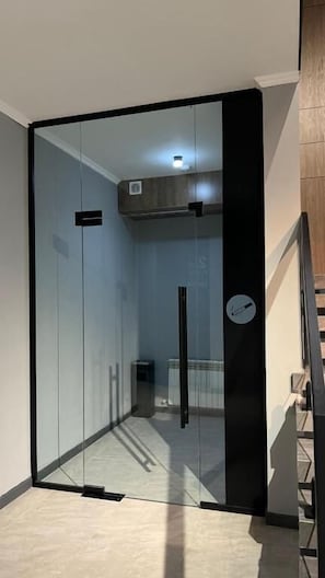 A modern room with a glass door leading to a hallway, a wooden staircase, and a small trash bin. - VanParkHotel (Shymkent)
