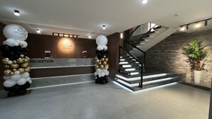 Un área de recepción con mostrador, escalera y una pared decorativa con un logotipo.
