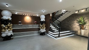 A reception area with a reception desk, a staircase, and a reception wall with a logo. - VanParkHotel (Shymkent)