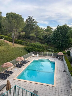 A rectangular swimming pool with a tiled deck, surrounded by a metal fence. There are lounge chairs and umbrellas along the poolside. - Luxury apartment, swimming pool, near the thermal baths (Gréoux-les-Bains)