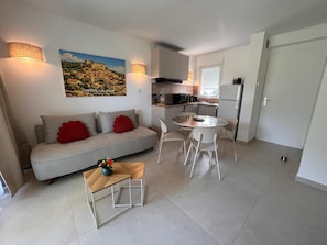 A compact living space with a sofa, a dining table with chairs, a kitchen area, and a painting on the wall. - Luxury apartment, swimming pool, near the thermal baths (Gréoux-les-Bains)