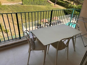 A balcony with a table and chairs, a view of a landscaped garden, and a pool in the background. - Vrbo Property (Gréoux-les-Bains)