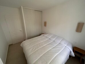 A bedroom with a bed, a door, a small table, and a wall-mounted light fixture. - Vrbo Property (Gréoux-les-Bains)