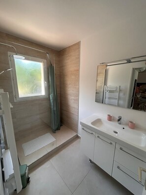 A bathroom with a shower, a sink with two pink cups, and a mirror above the sink. - Vrbo Property (Gréoux-les-Bains)