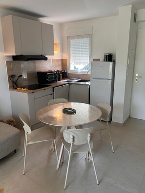 A compact kitchen with a dining area, a built-in oven, a refrigerator, and a window with blinds. - Luxury apartment, swimming pool, near the thermal baths (Gréoux-les-Bains)