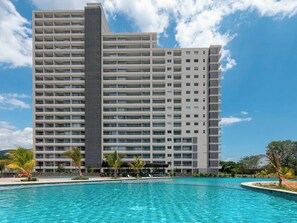 Ein Hochhaus-Hotel mit mehreren Balkonen, einem Schwimmbad und tropischer Bepflanzung.