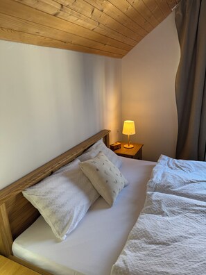A neatly made bed with a wooden headboard, a bedside lamp, and a pillow with a floral pattern. - Vrbo Property (Gornji Orašac)