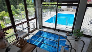 A view of a swimming pool from a balcony with a glass railing, a small hot tub, and a statue of a mermaid. - Vrbo Property (Gornji Orašac)